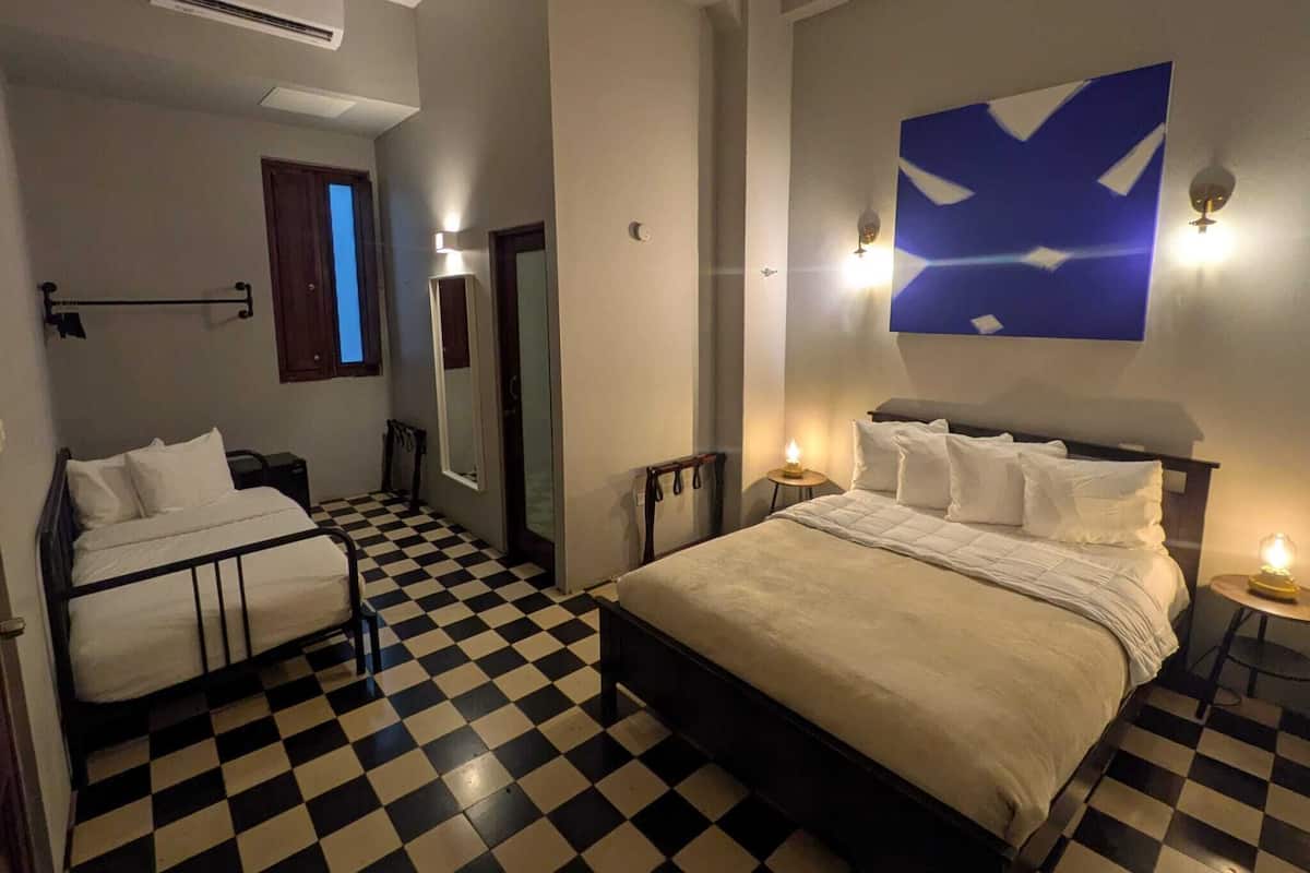 Hotellihuone, jossa on ruutukuviollinen lattia, kaksi sänkyä, suuri seinämaalaus ja ilmastointilaite.