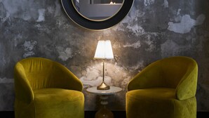 A room with a textured wall, a round mirror, a table with a lamp, and two armchairs.