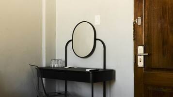 A compact room with a black desk, a chair, a mirror, and a wooden door.
