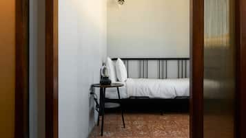 Ein kleiner, schmaler Raum mit einem Bett, einem Tisch und einer Wandlampe.