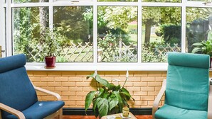 A room with two chairs, a small table with a plant and a tray, and a window with a view of a garden. - A wonderful three bedroom cottage sleeping six. (Hartlebury, near Kidderminster)