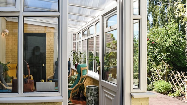 A conservatory with a brick wall, wooden shutters, and a view of the garden. - A wonderful three bedroom cottage sleeping six. (Hartlebury, near Kidderminster)