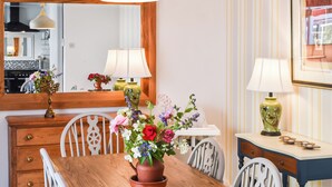 A dining area with a wooden table, white chairs, a mirror, and a vase of flowers. - A wonderful three bedroom cottage sleeping six. (Hartlebury, near Kidderminster)