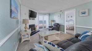 A living room with a television, a fireplace, a sofa, and a bed with a view of the sea.