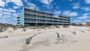 A multi-story hotel with balconies, situated on a sandy beach with a clear sky.