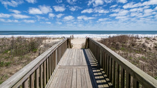 A wooden boardwalk leading to a beach with a clear sky.