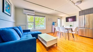 Una sala moderna con un sofá azul, una mesa de centro blanca y un comedor con sillas blancas.