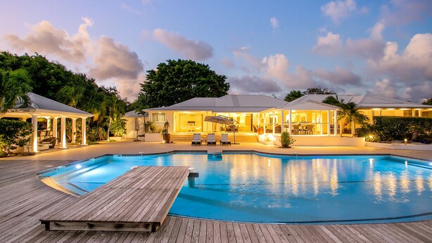 Ein Pool mit Holzterrasse, eine überdachte Terrasse und ein Haus mit großen Fenstern und einer überdachten Sitzgruppe.