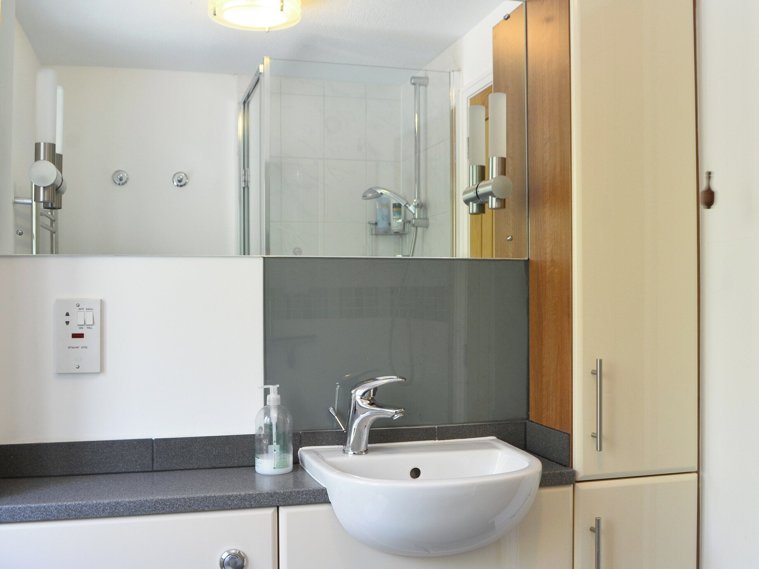 A modern bathroom with a white sink, a mirror, and a shower.