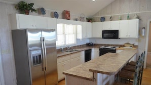 A kitchen with white cabinets, a stainless steel refrigerator, a microwave, and a wooden island with bar stools.