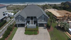 A two-story house with a front porch, a covered patio, and a view of the beach.