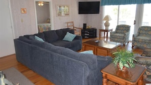 A living room with a sectional sofa, a television, a small table with a plant, and patterned armchairs.
