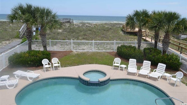 A pool area with lounge chairs and palm trees, overlooking a beach and ocean.