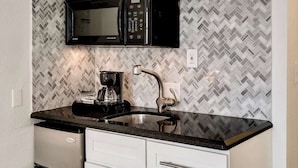 A compact kitchen with white cabinets, a black microwave, a stainless steel refrigerator, and a herringbone-patterned backsplash. - Best Beach Location | Wi-Fi, TV & Amenities (Miami Beach)