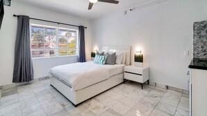 A modern bedroom with a bed, nightstands, a ceiling fan, and a window with curtains. - Best Beach Location | Wi-Fi, TV & Amenities (Miami Beach)