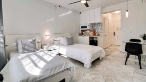Un dormitorio moderno con dos camas, un ventilador de techo, una zona de cocina y una mesa de comedor.