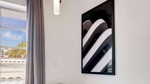A modern room with a white table, two black chairs, a grey curtain, and a large abstract painting on the wall. - Best Beach Location | Wi-Fi, TV & Amenities (Miami Beach)