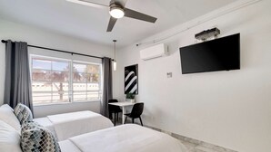 A hotel room with two beds, a desk, a chair, a ceiling fan, a TV, and a window with curtains. - Best Beach Location | Wi-Fi, TV & Amenities (Miami Beach)