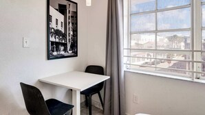 A room with a white table and two black chairs, a black and white photograph on the wall, and a window with a view of buildings. - Best Beach Location | Wi-Fi, TV & Amenities (Miami Beach)