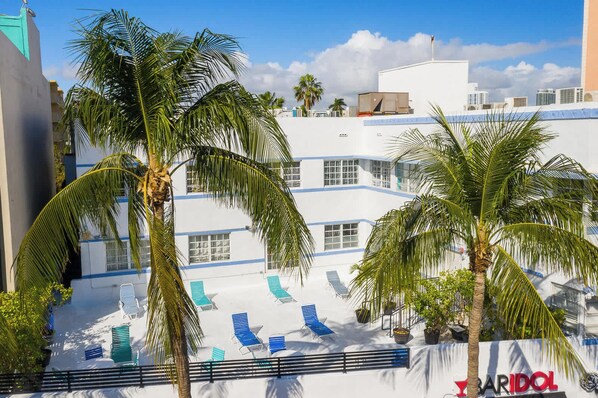 A hotel with a white facade, blue accents, and a pool area with lounge chairs.