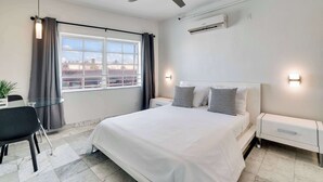 A modern hotel room with a large bed, a desk with a chair, a ceiling fan, and a window with curtains. - Best Beach Location | Wi-Fi, TV & Amenities (Miami Beach)