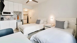 Une chambre d’hôtel avec deux lits, un coin cuisine, un ventilateur de plafond et un four à micro-ondes.