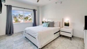 Un dormitorio moderno con una cama grande, una mesita de noche, un ventilador de techo y una ventana con cortinas.