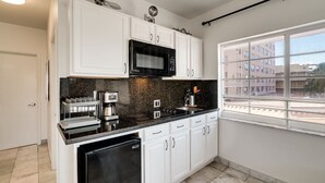 A modern kitchen with white cabinets, a black countertop, a built-in microwave, and a coffee maker. - Best Location SOBE Top Floor 2 min to beach & fun (Miami Beach)