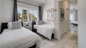 A hotel room with two beds, a ceiling fan, a window with curtains, a bedside table with a lamp, and a door leading to another room. - Best Location SOBE Top Floor 2 min to beach & fun (Miami Beach)