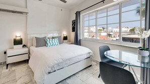 Un dormitorio con cama, mesita de noche y ventana que ofrece vistas a edificios.