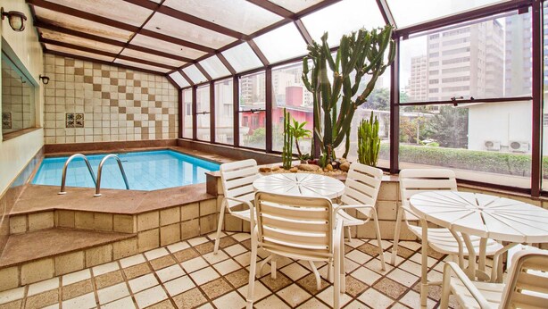 Uma sala de estar com janelas amplas, piscina, cadeiras brancas.