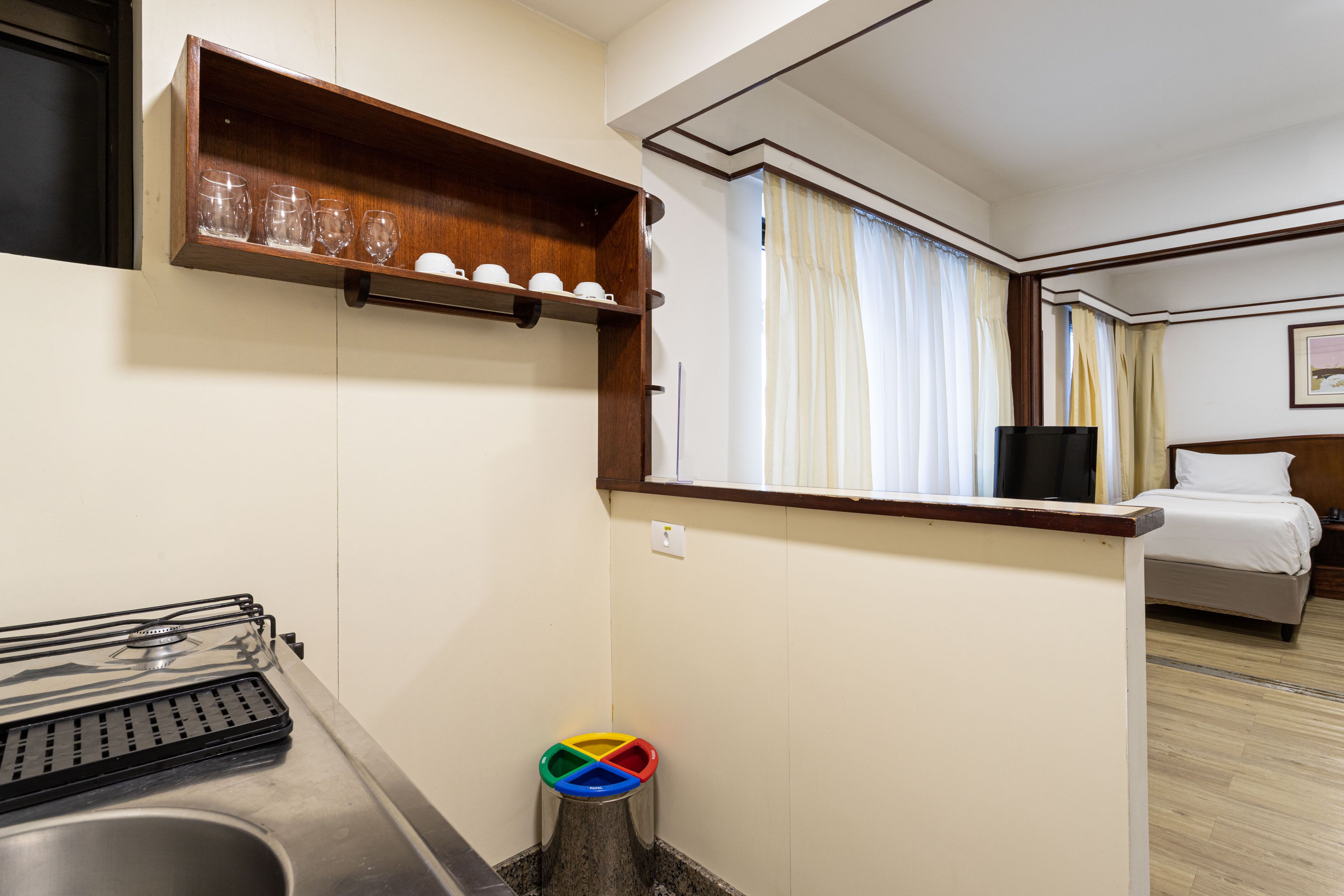 A hotel room with a bed, a small bathroom with a sink, a mirror, and a shelf with glasses.