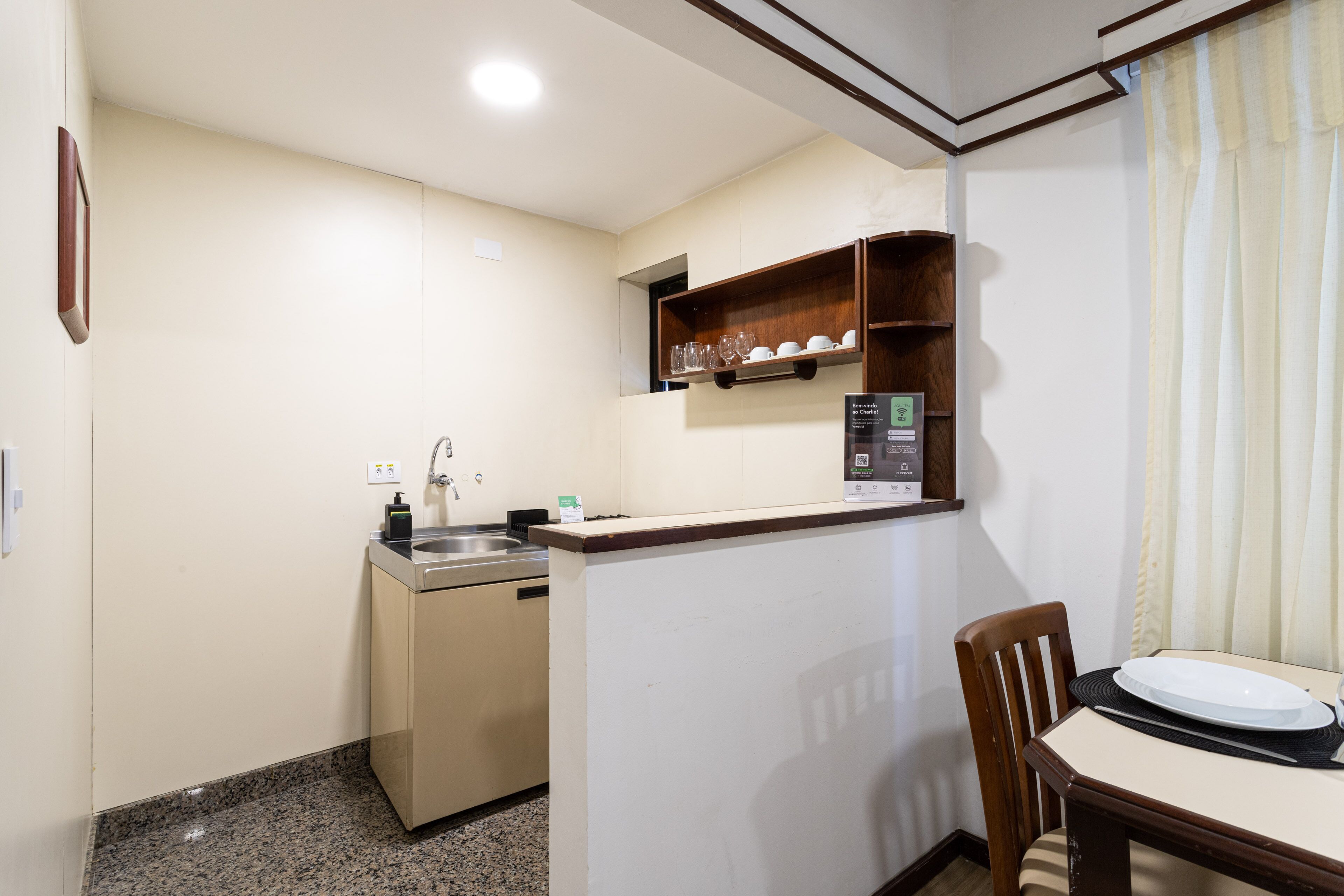 A compact kitchen with a built-in dishwasher, a small shelf with glasses, and a dining area with a table and chairs.