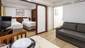 Quarto de hotel com televisão, duas camas, um sofá, uma mesa de jantar com pratos e talheres, e um quadro na parede.
