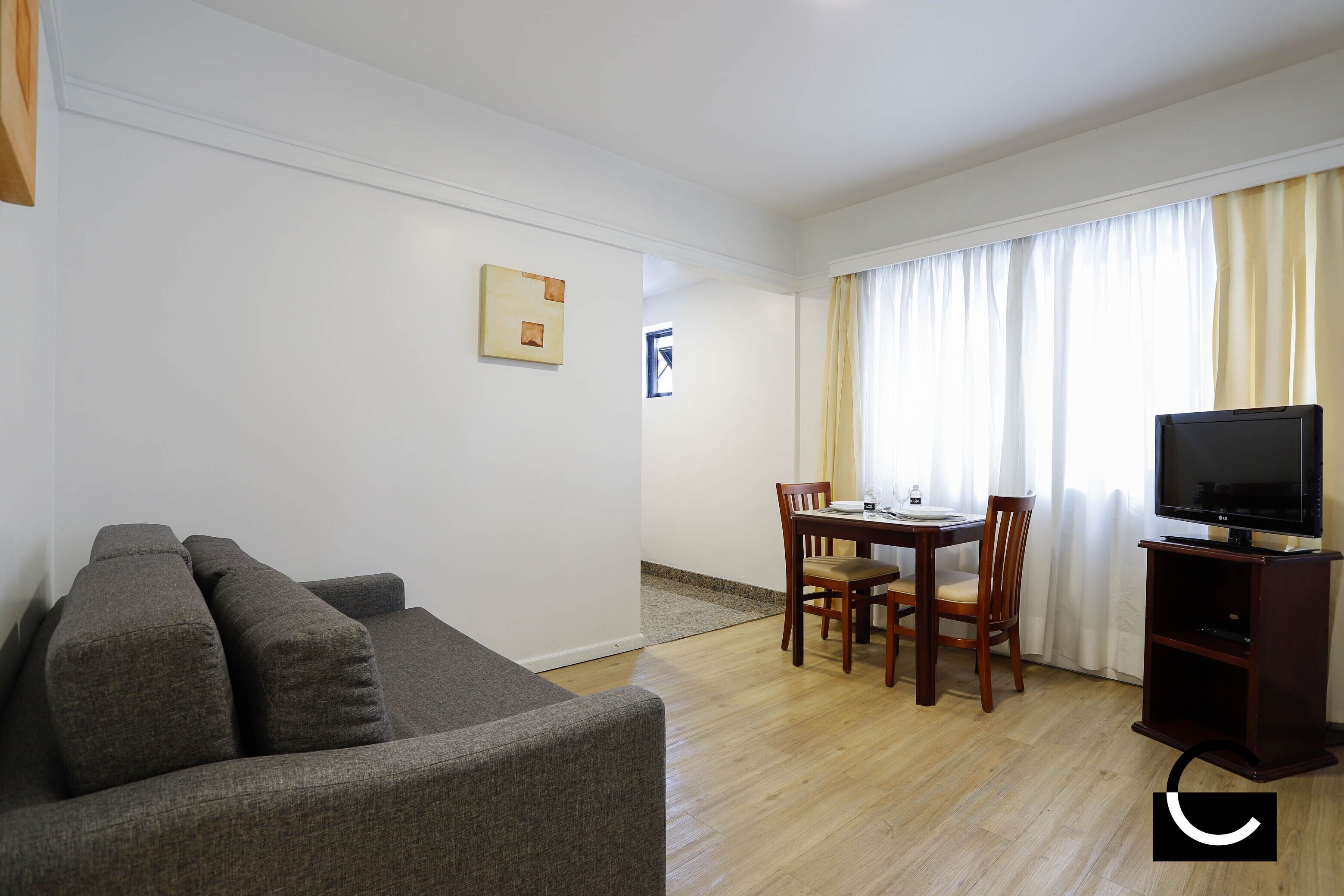 A living room with a sofa, a dining table with chairs, a television, and a window with curtains.