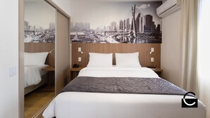 Quarto de hotel com uma cama grande, um mural com vista para a cidade na parede, cabeceira de madeira e aparelho de ar condicionado.