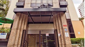 Um edifício alto com design moderno, apresentando uma grande fachada de vidro e um conjunto de degraus que levam à entrada.