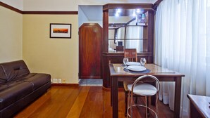 Um espaço compacto com uma mesa de jantar de madeira para dois, um sofá de couro e um quadro na parede.