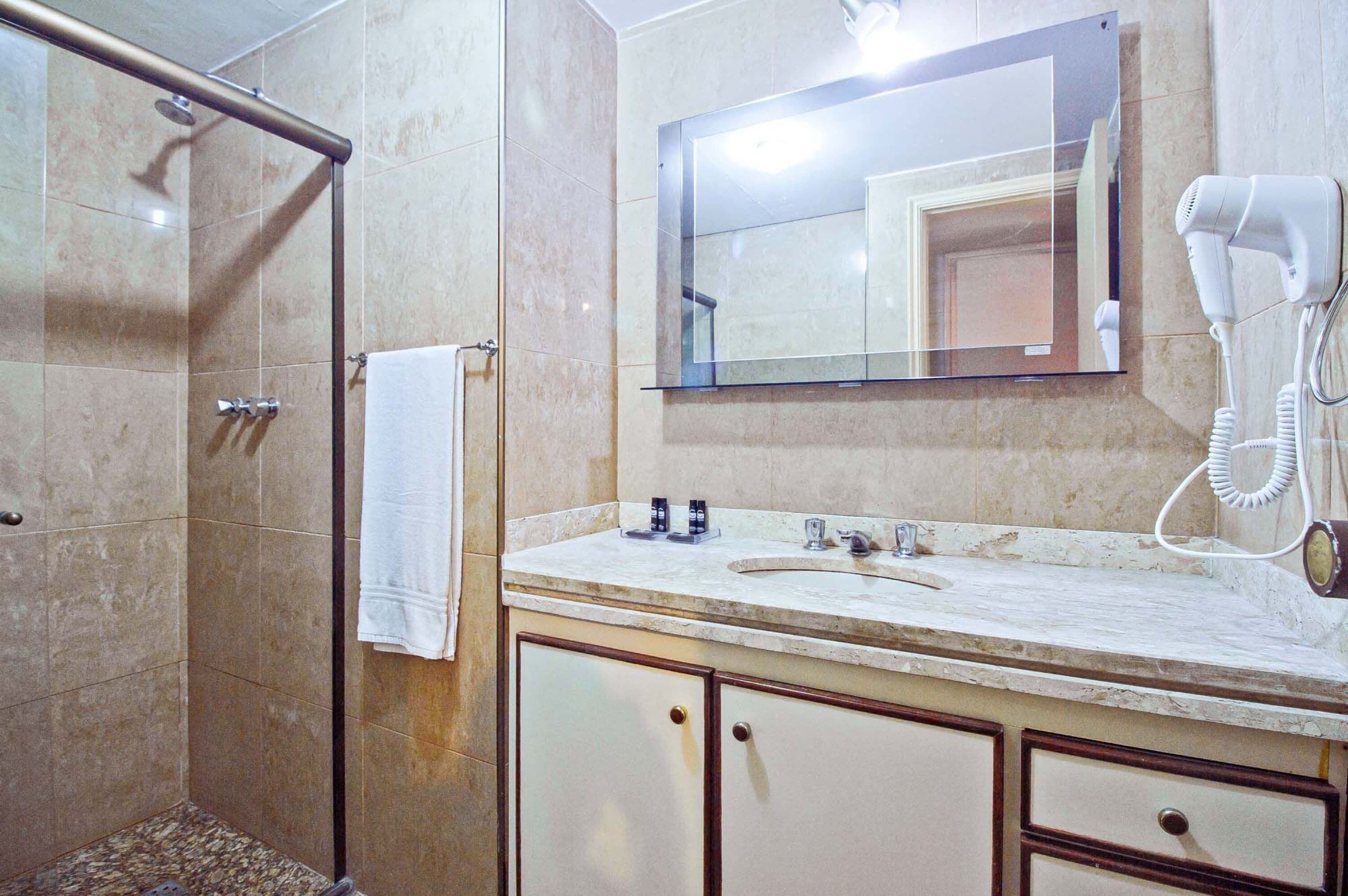A bathroom with a shower, a sink, a mirror, and a hairdryer.