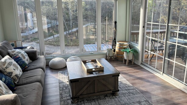 A cozy living room with a large window, a wooden coffee table, a sofa with patterned cushions, and a decorative wall piece.
