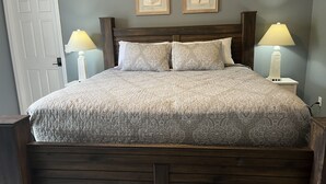 A bed with a patterned bedspread, two bedside lamps, and two framed pictures on the wall.