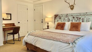 Ein Schlafzimmer mit einem Bett, einem Schreibtisch, einem Stuhl und einem an der Wand befestigten Hirsch-Dekoration.
