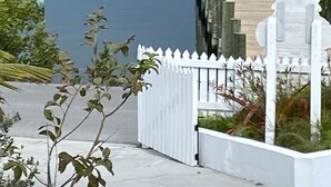 Una proprietà sul lungomare con un molo di legno, un recinto di legno bianco e un piccolo edificio bianco con tetto rosa.