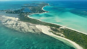 Vista aérea de una zona costera con una playa arenosa, aguas turquesas cristalinas y una densa área boscosa.