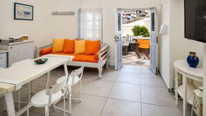 A modern living room with a white sofa, orange cushions, a dining table with chairs, and a TV mounted on the wall. - Day One Fira Mansion (Santorini)