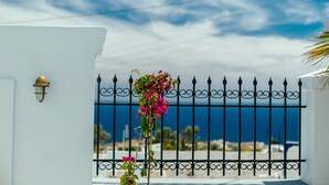 A white building with a black wrought iron gate, a clear blue sky, and a view of the sea. - Day One Fira Mansion (Santorini)