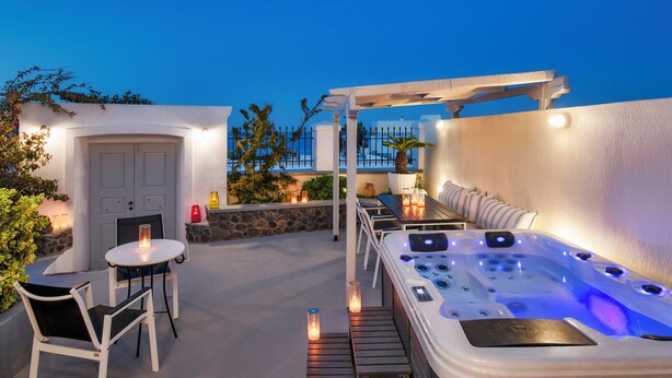 An outdoor patio with a hot tub, seating area, and a door. - Day One Fira Mansion (Santorini)
