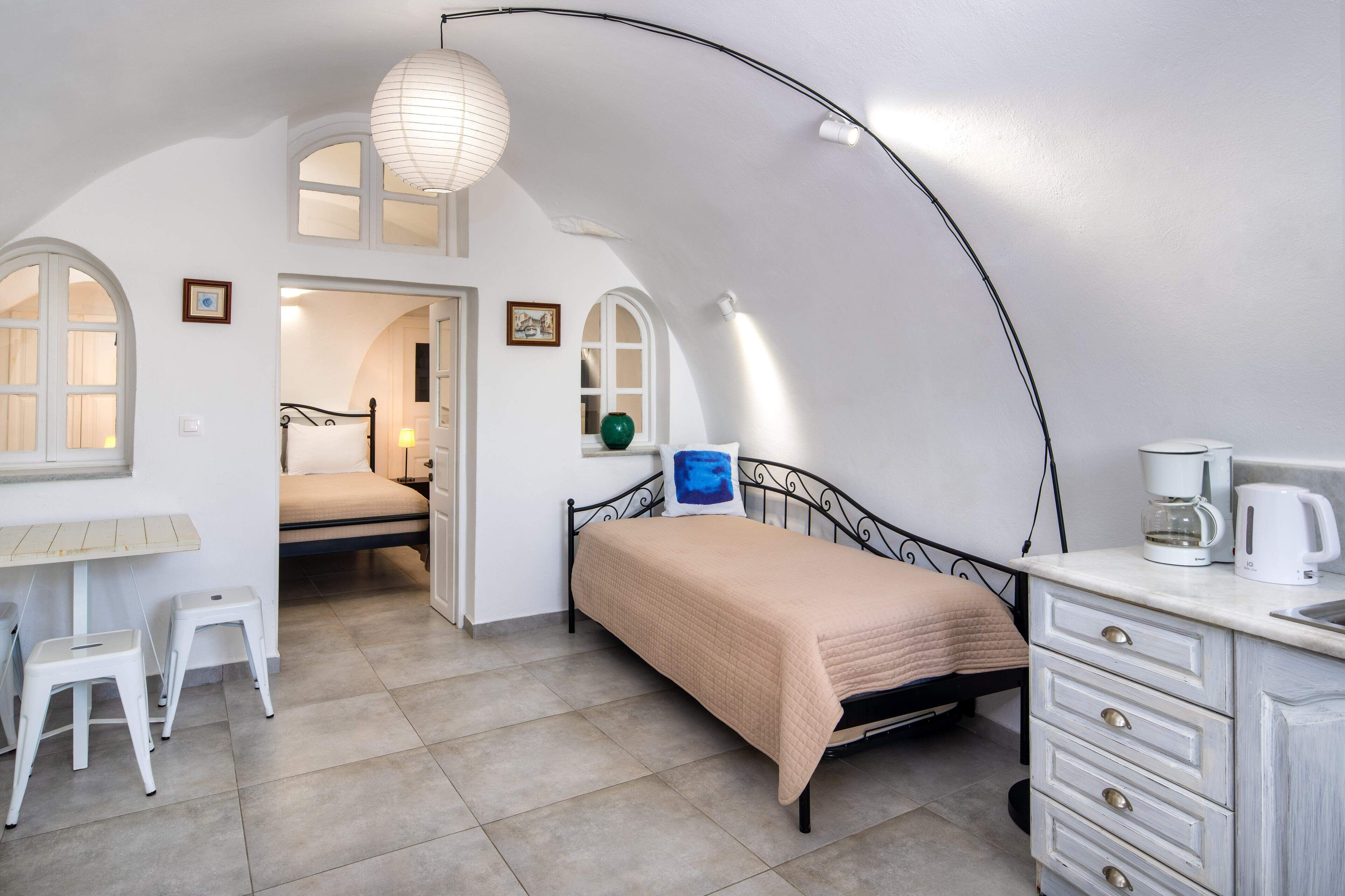 A bedroom with a bed, a desk, a chair, and a kitchenette.
