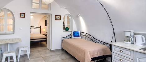 A bedroom with a bed, a desk, a chair, and a kitchenette.