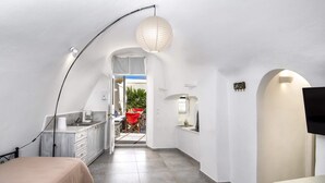 A narrow hallway with a bed on the left, a kitchenette on the right, and a TV mounted on the wall. - Day One Fira Mansion (Santorini)